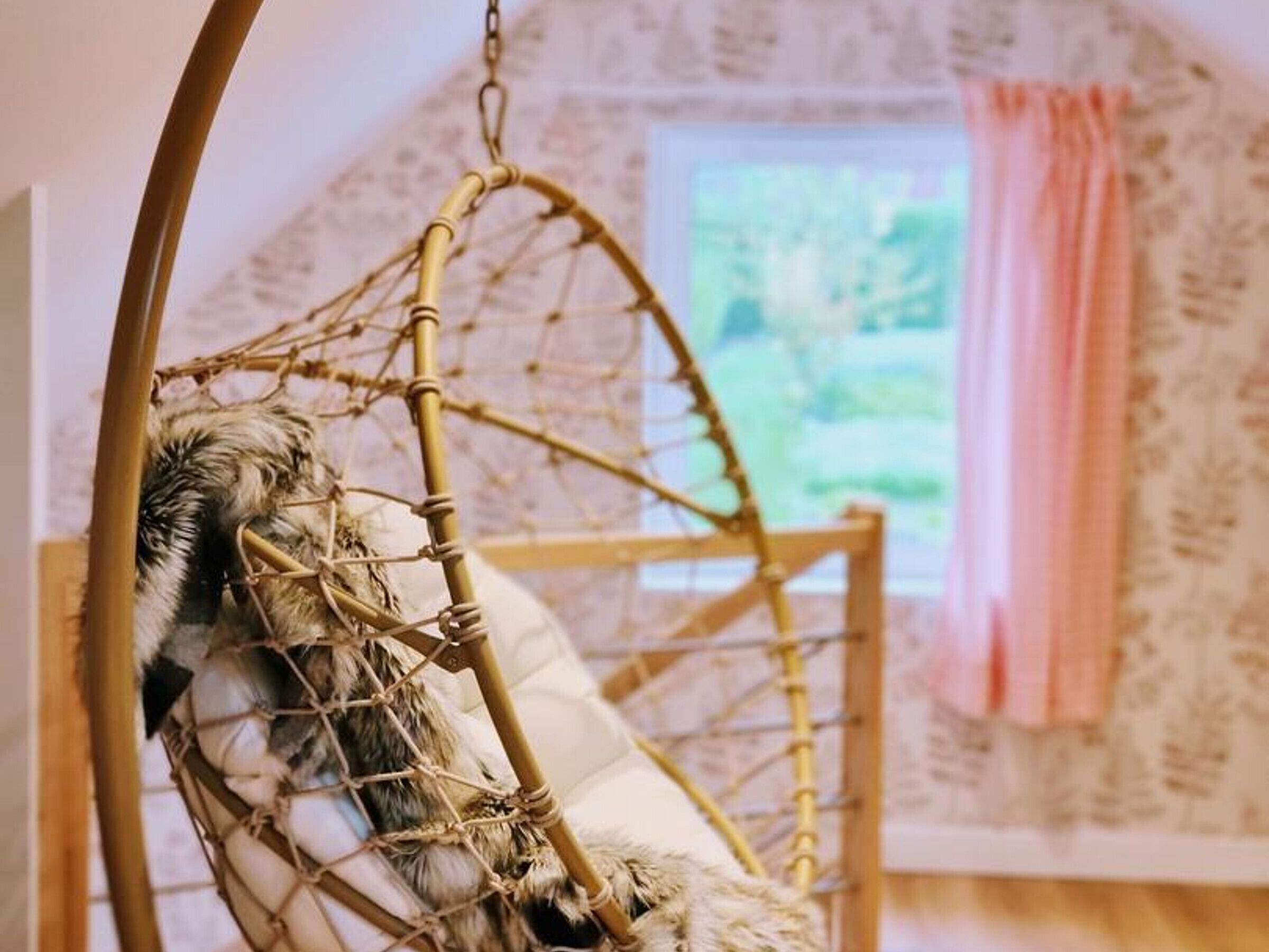 Una stanza con una poltrona amaca, una finestra con tenda e un muro decorato con un motivo floreale.