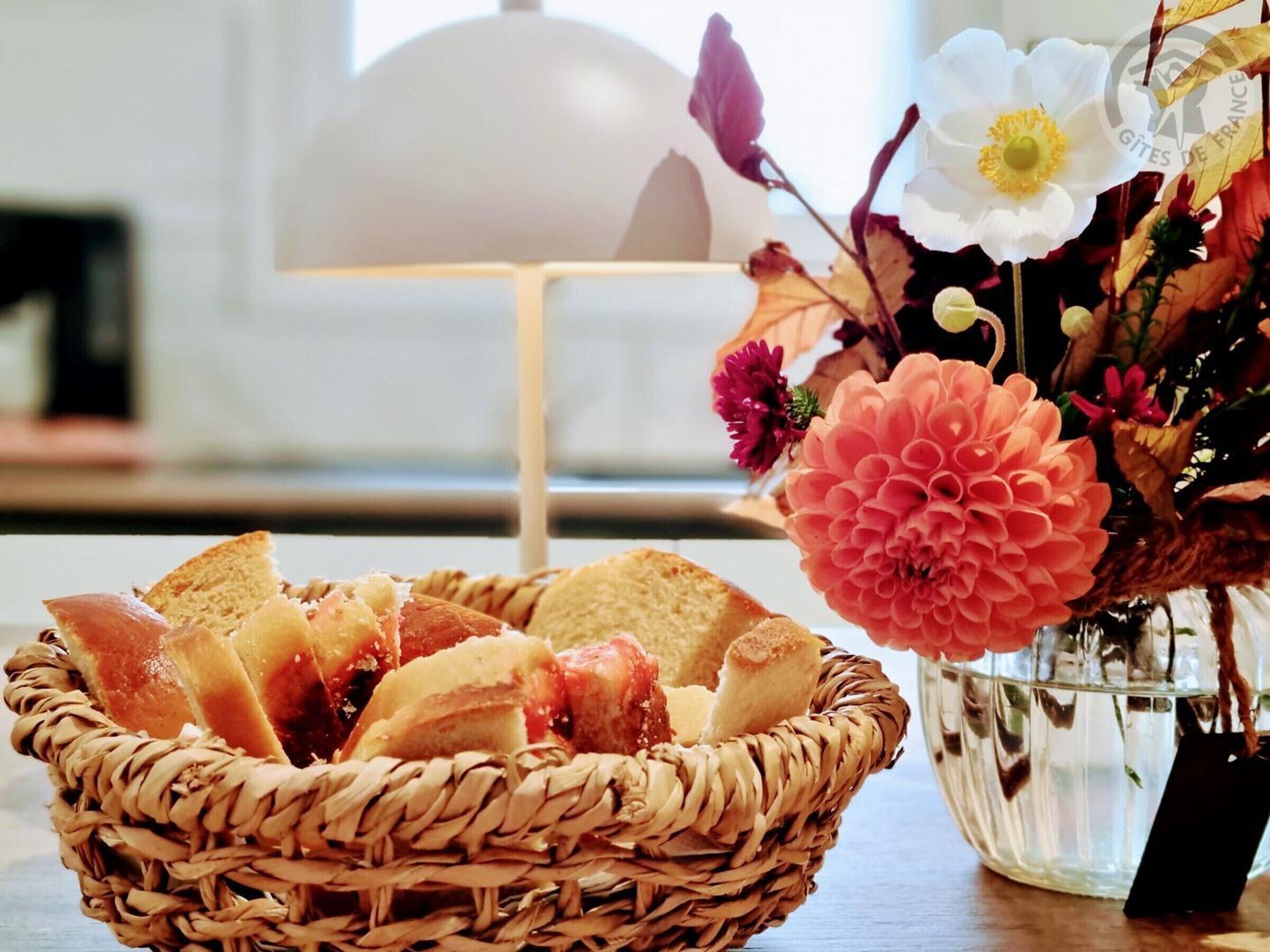 A wicker basket filled with bread and a vase with flowers on a table.