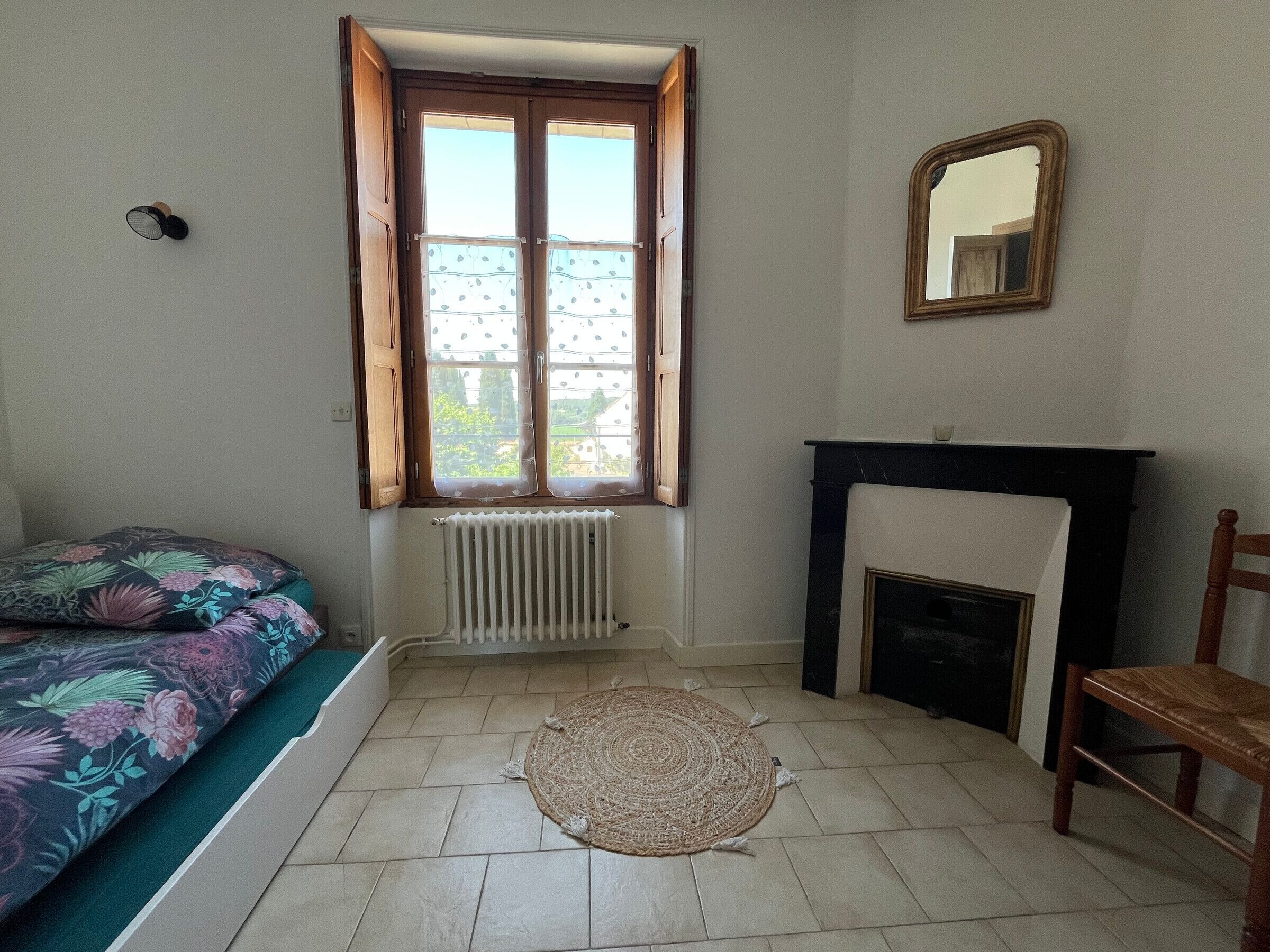 A bedroom with a bed, a fireplace, a mirror, and a window with curtains.