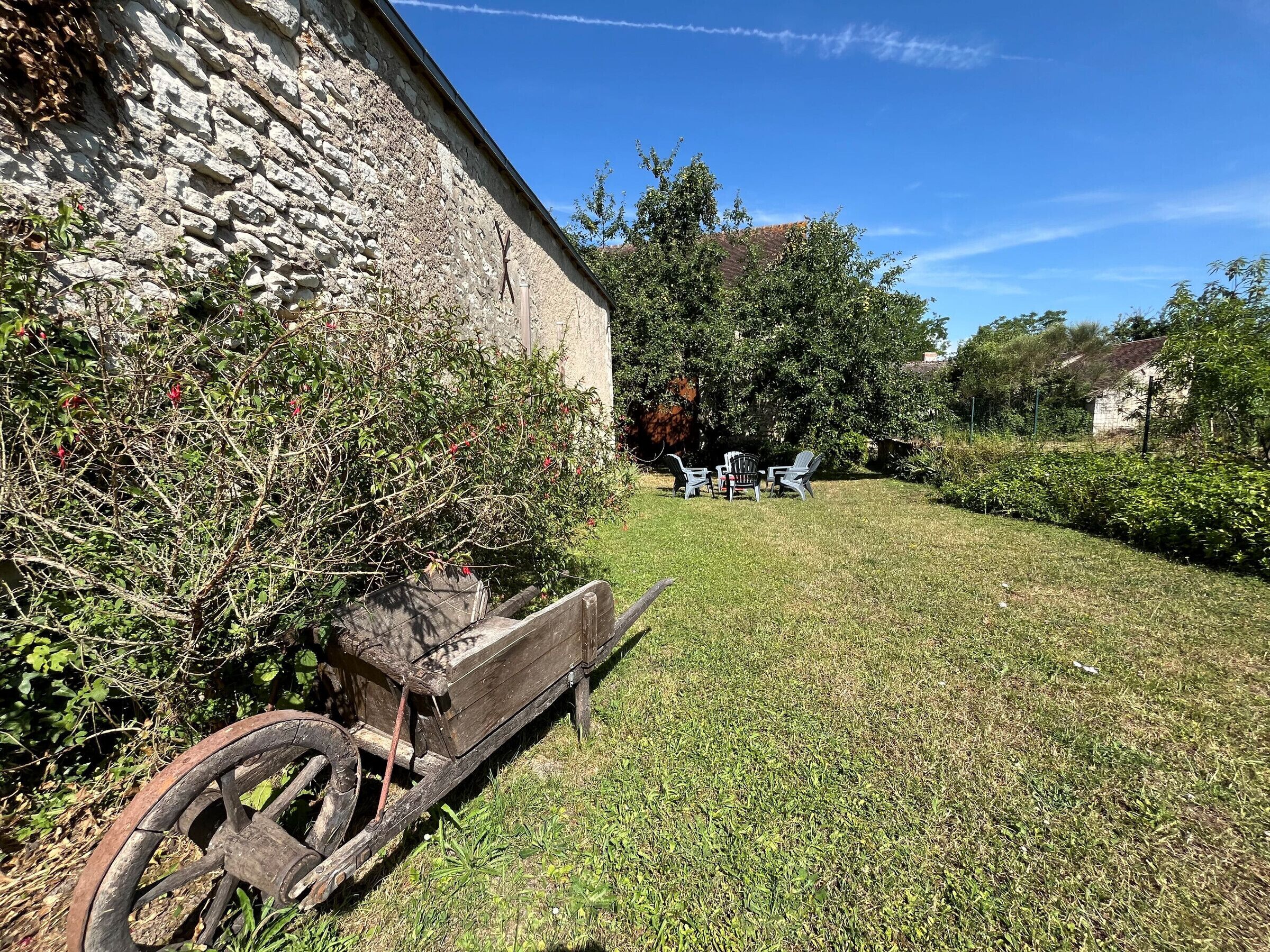 Un espace verdoyant avec un chariot en bois, un mur de pierre et des sièges extérieurs.