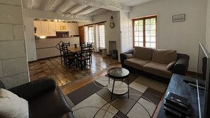 A living room with a sofa, a coffee table, and a TV stand. There is a dining area with a table and chairs. The room has a tiled floor and a ceiling with exposed beams. - Quiet cottage, pets allowed, parking - 6 guests (Chambon)