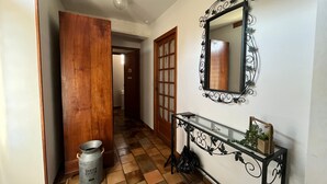 A hallway with a tiled floor, a wooden door, a metal trash can, a console table with a mirror, and a wall-mounted decorative mirror. - Quiet cottage, pets allowed, parking - 6 guests (Chambon)