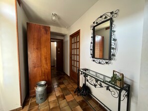 Ein Flur mit gefliestem Boden, einer Holztür, einem Metallmülleimer, einem Konsolentisch mit Spiegel und einem an der Wand befestigten Zier-Spiegel.