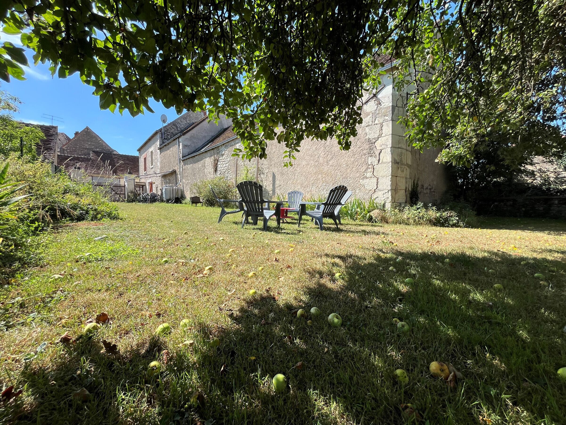 A grassy outdoor area with three Adirondack chairs, a stone building, and a clear sky.