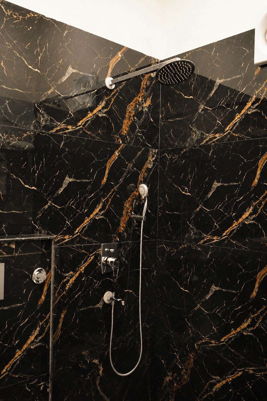 Un baño con pared de mármol negro, un cabezal de ducha de mano y un grifo empotrado.