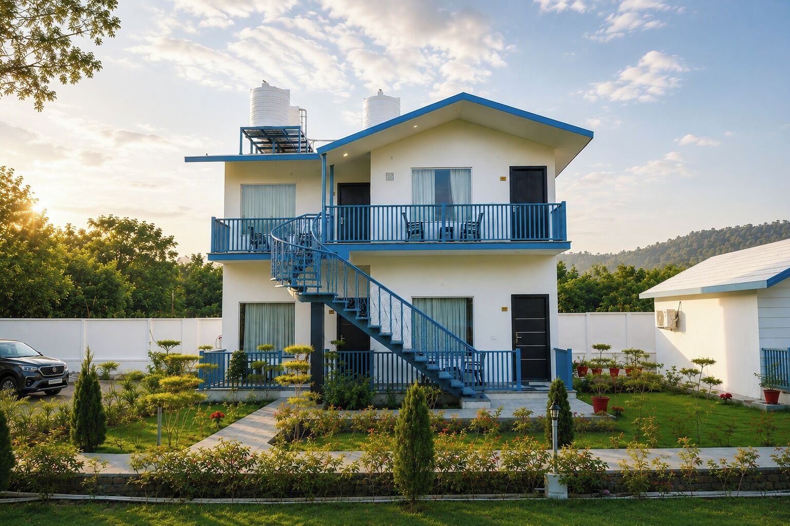 A two-story building with a blue staircase, a balcony, and a garden with various plants.