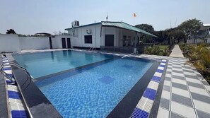Piscina com borda quadriculada, edifício com telhado verde e uma bandeira.