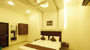 A hotel room with a bed, bedside tables, a wardrobe, a ceiling fan, and a wall-mounted picture. - Corbett Vantara (Ramnagar)