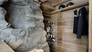 Ein rustikaler Raum mit Steinwand, Holzbalken und einem Regal mit Helmen und Jacken.