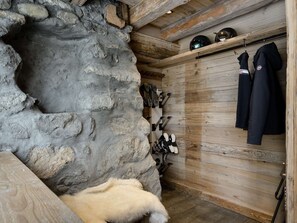 A rustic room with a stone wall, wooden beams, and a shelf with helmets and jackets. - Chalet in Courchevel 1850, 8 guests, ski-in/ski-out, sauna, Wifi (Courchevel)