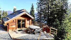 Eine Holzhütte mit geneigtem Dach, einer Terrasse mit Picknicktischen und einem Kiesgrund.