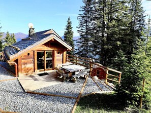 A wooden cabin with a sloped roof, a deck with picnic tables, and a gravel ground. - Chalet in Courchevel 1850, 8 guests, ski-in/ski-out, sauna, Wifi (Courchevel)