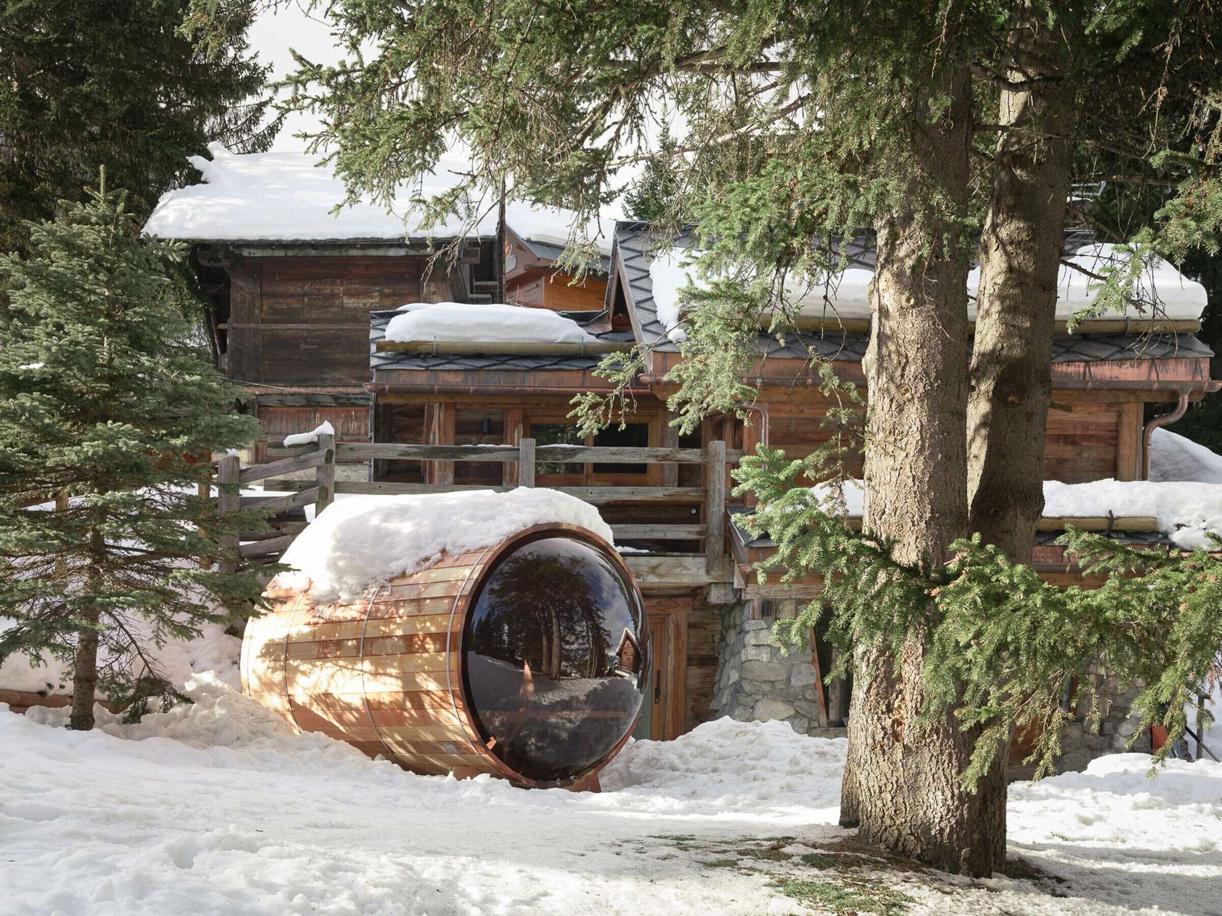 Une cabane en bois avec un toit enneigé, un tonneau en bois et un mur de pierres.