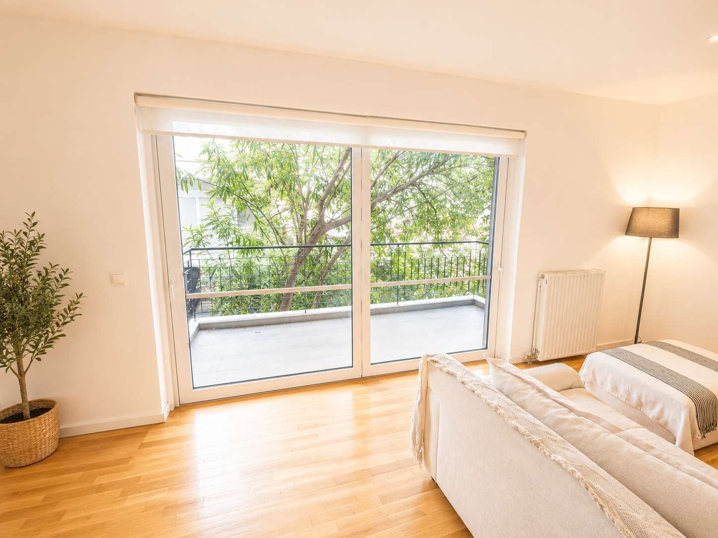 A bedroom with a large sliding glass door to a balcony, a bedside table, a lamp, and a potted plant.