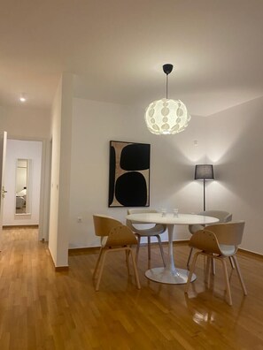 A dining area with a round table, four chairs, a hanging light fixture, and a wall-mounted abstract painting. - Premium 3 Bd Retreat in Neapoli-Lycabettus (Athina)