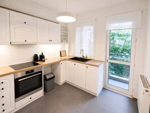 A modern kitchen with white cabinetry, a black stove, and a window with a view of greenery. - Premium 3 Bd Retreat in Neapoli-Lycabettus (Athina)