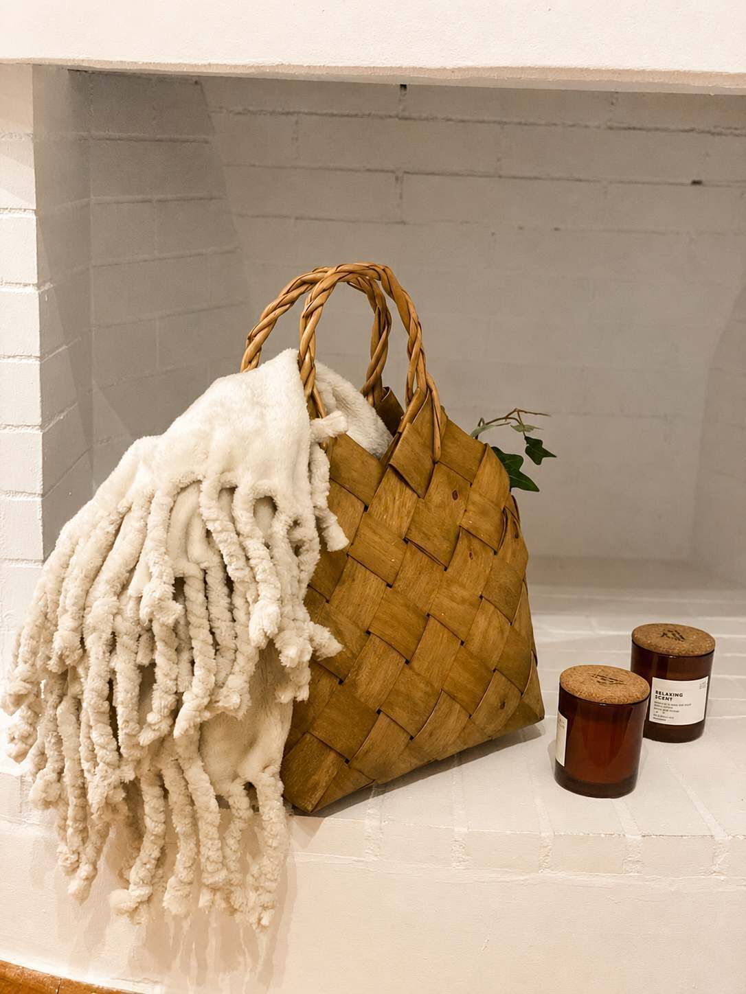 A woven basket with a white fluffy item inside, placed on a white surface with two candles labeled 'Relaxing Scents' beside it.