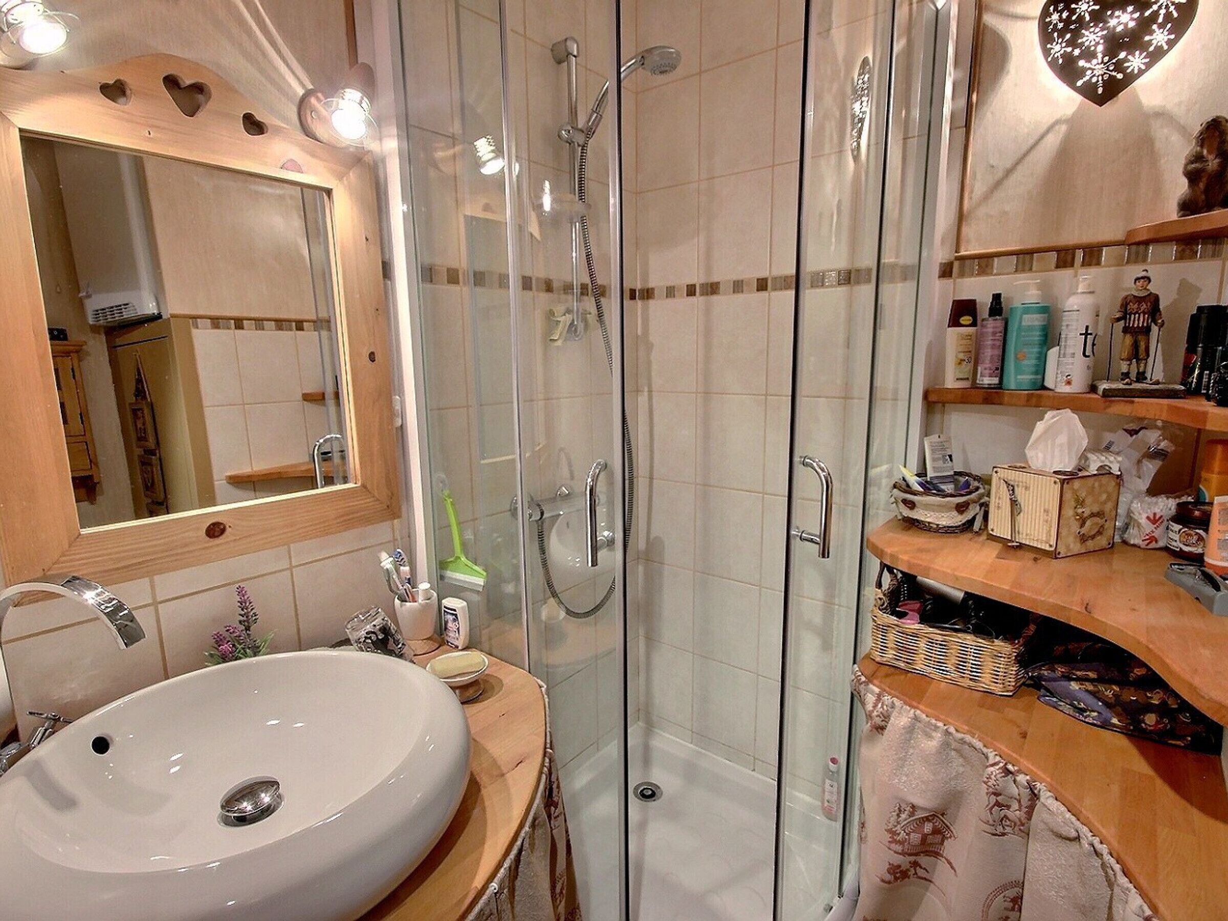 A bathroom with a glass-enclosed shower, a sink with a mirror above it, and a wooden vanity with toiletries.