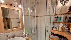 Ett badrum med en dusch som är avskärmad med glasväggar, ett handfat med en spegel ovanför och en träinredd tvättställsmöbel med plats för toalettartiklar.