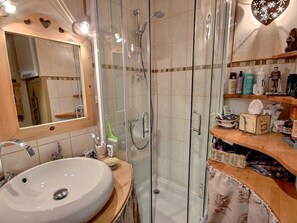 A bathroom with a glass-enclosed shower, a sink with a mirror above it, and a wooden vanity with toiletries. - Studio near funicular - 4 guests (Bourg-Saint-Maurice)