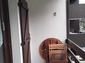 A wooden door with a circular cutout on the wall, a small sensor on the wall, and a stack of wooden chairs leaning against the wall. - Studio near funicular - 4 guests (Bourg-Saint-Maurice)