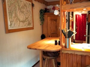 A wooden table with a map, a cabinet, and a mirror with a red curtain. - Studio near funicular - 4 guests (Bourg-Saint-Maurice)