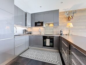 A modern kitchen with grey cabinets, a built-in oven, and a patterned rug. - Spacious apartment, central location - 8 guests (Le Corbier)