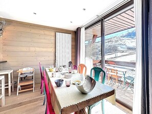 A dining area with a large table, chairs, and a view of a snowy landscape through a large window. - Spacious apartment, central location - 8 guests (Le Corbier)