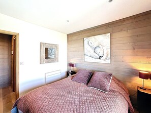 A bedroom with a bed, a nightstand, a lamp, and two wall-mounted paintings. - Spacious apartment, central location - 8 guests (Le Corbier)