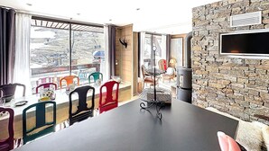 En matplats med ett bord och stolar, en vägg av sten, en väggmonterad tv och ett fönster med utsikt över ett bergigt landskap.