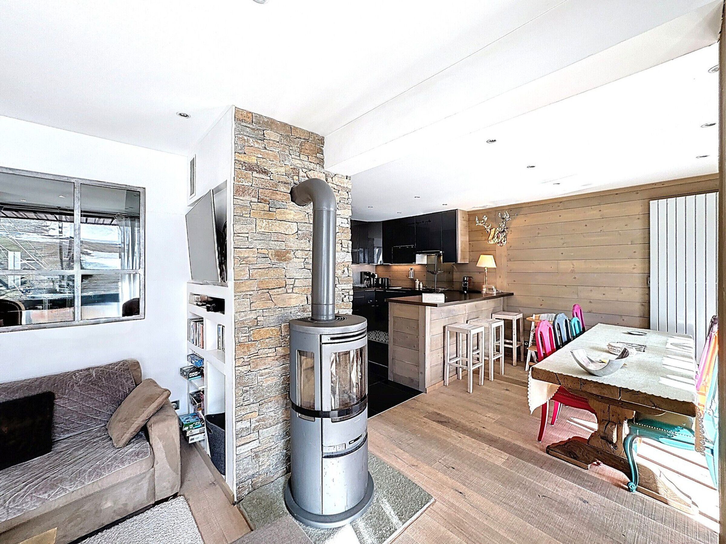 A modern living space with a stone fireplace, a kitchen area, and a dining table with bar stools.