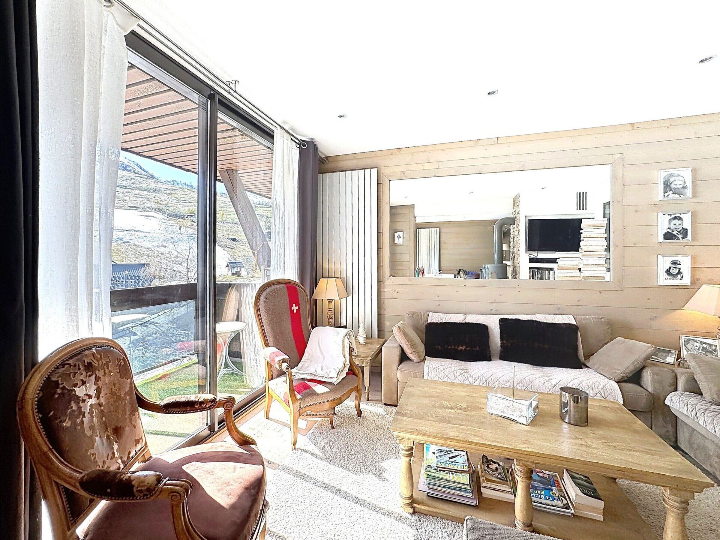 A room with a large window, a sofa, a wooden coffee table, and a chair with a red cushion.