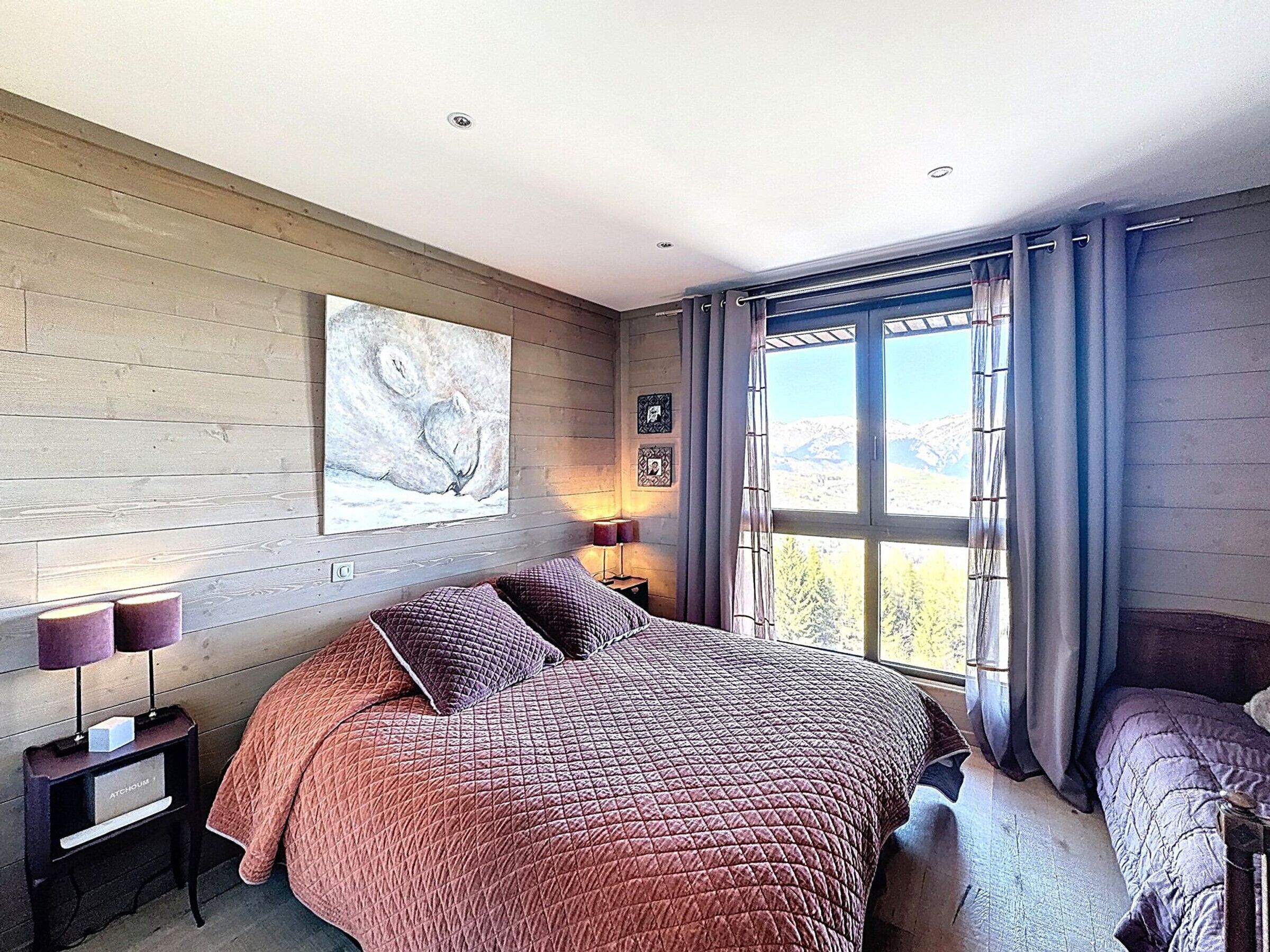 A bedroom with a large bed, a nightstand, a lamp, and a window with curtains.