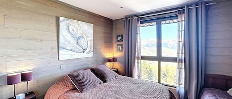 A bedroom with a large bed, a nightstand, a lamp, and a window with curtains.