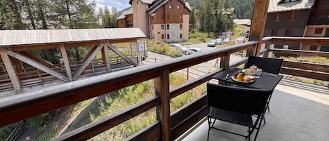 A balcony with a table set for dining, overlooking a mountainous landscape with traditional buildings.
