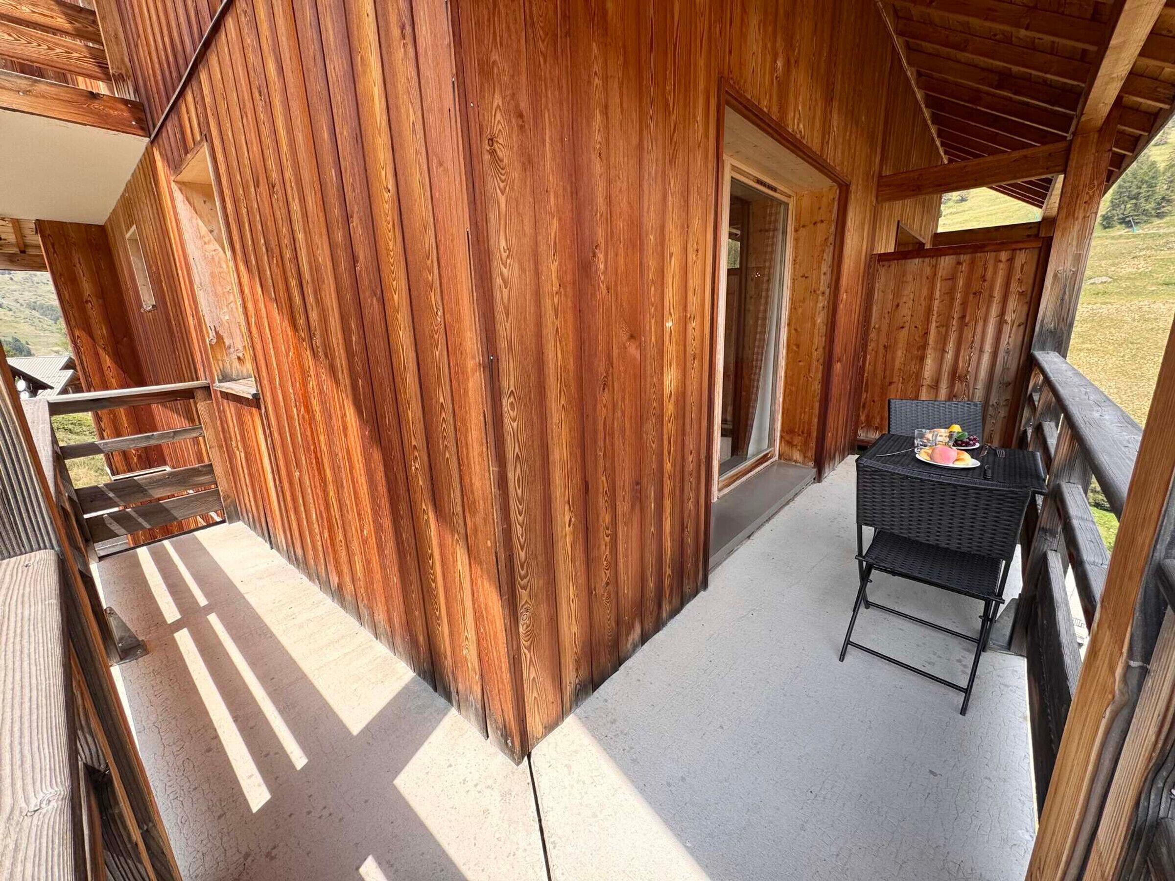 Eine Holzblockhütte mit einem Balkon, einem Tisch mit Teller und Glas sowie einer Tür zu einem Innenraum.