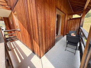 Eine Holzblockhütte mit einem Balkon, einem Tisch mit Teller und Glas sowie einer Tür zu einem Innenraum.