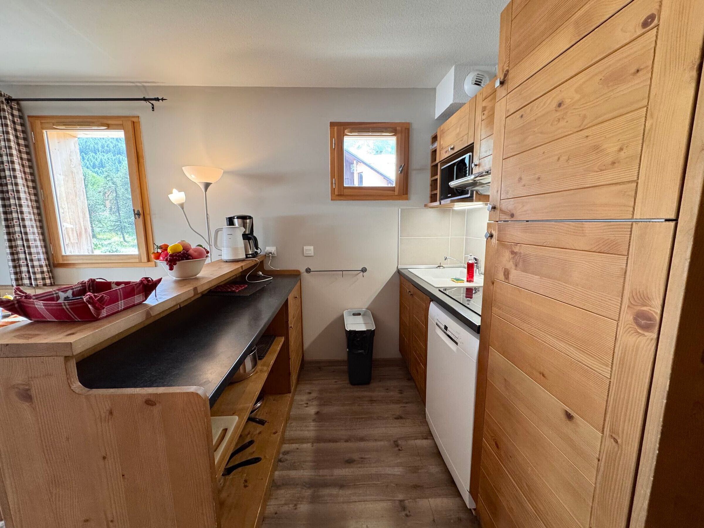 A compact kitchen with wooden cabinetry, a countertop, a sink, a dishwasher, and a window providing natural light.