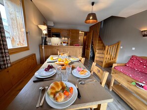 Ein Essbereich mit einem Holztisch, gedeckt für eine Mahlzeit, eine Küche im Hintergrund und eine Treppe, die zu einer anderen Ebene führt.