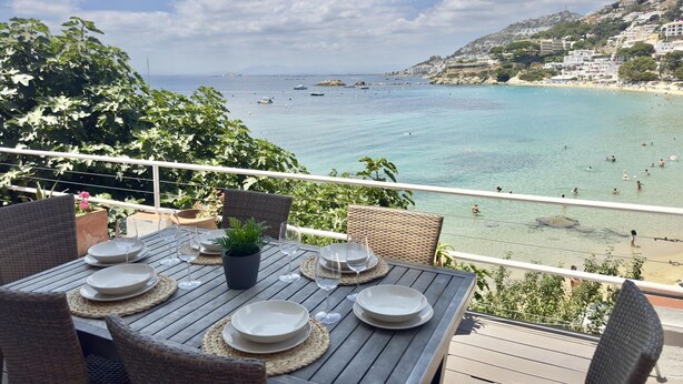 A terrace with a table set for dining, overlooking a beach with boats and people. - Air-conditioned apartment with beach access and terrace in Roses (Roses)