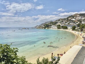 Uma praia costeira com águas claras, areal arenoso e edifícios numa encosta.