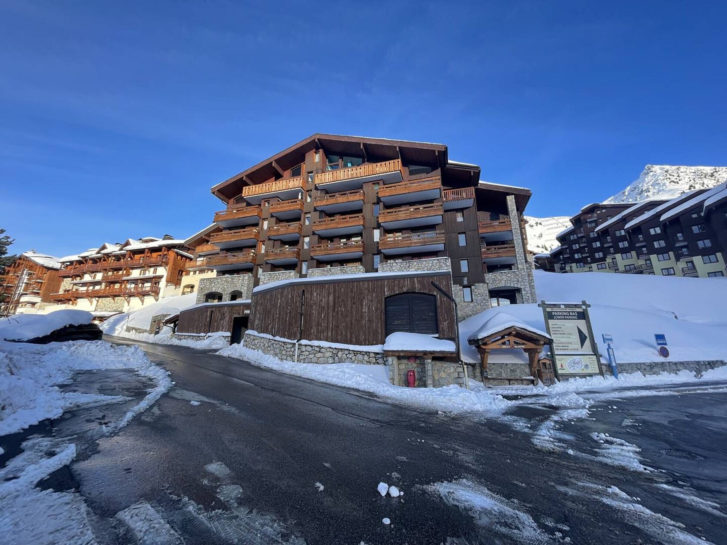 Un immeuble à plusieurs étages doté de balcons, d’une façade en pierre et situé dans un environnement enneigé.