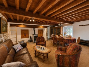 A cozy living room with a fireplace, wooden ceiling beams, a dining area with a table set for four, and a comfortable seating arrangement. - Typical house, pets welcome - 6 guests (Chalmazel-Jeansagnière)
