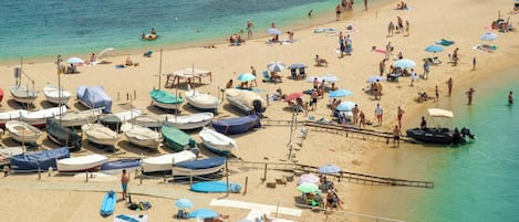 A beach with boats, umbrellas, and people.