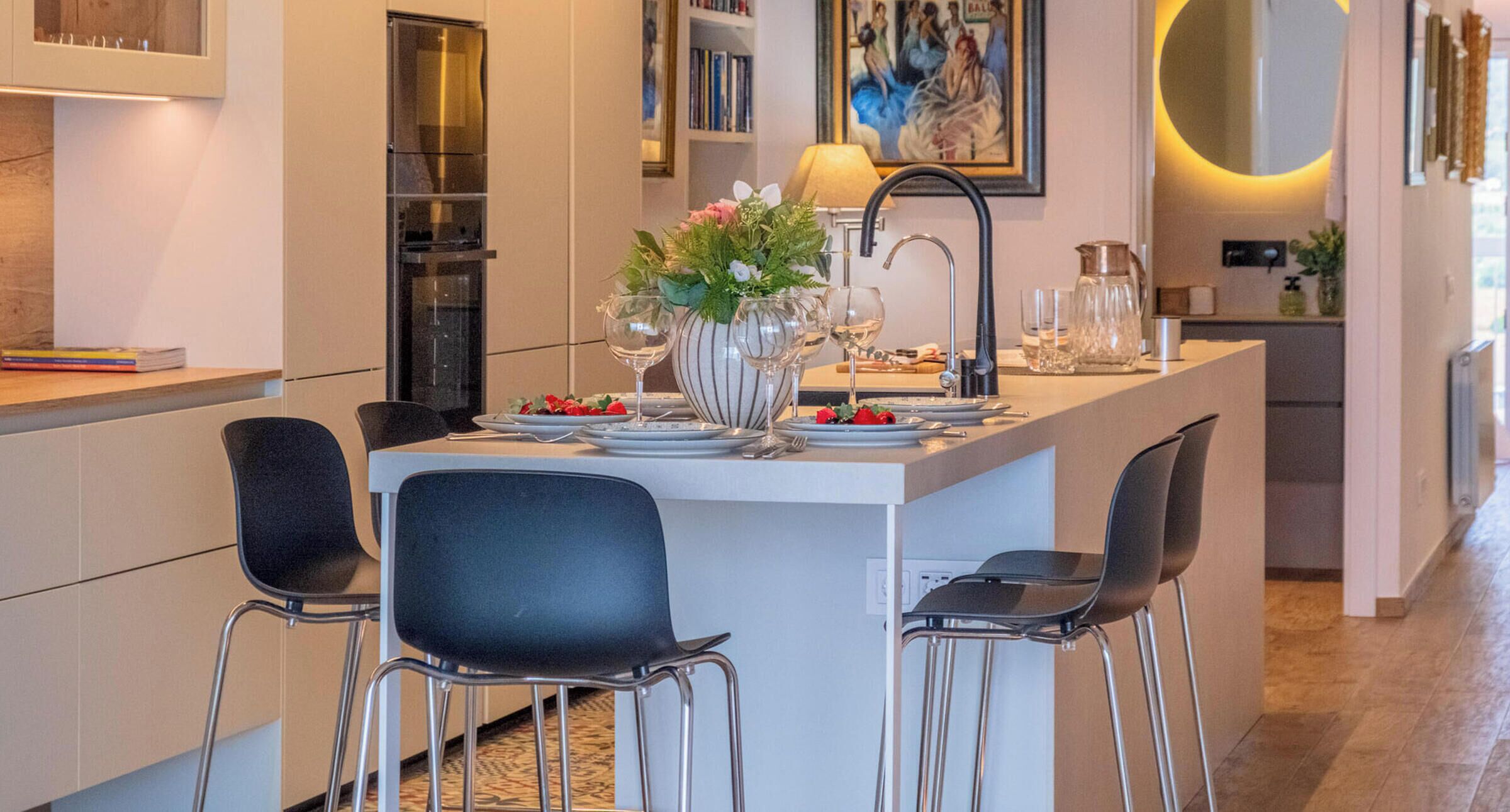 Una cocina moderna con una isla central, taburetes de bar, una mesa de comedor y un cuadro en la pared.