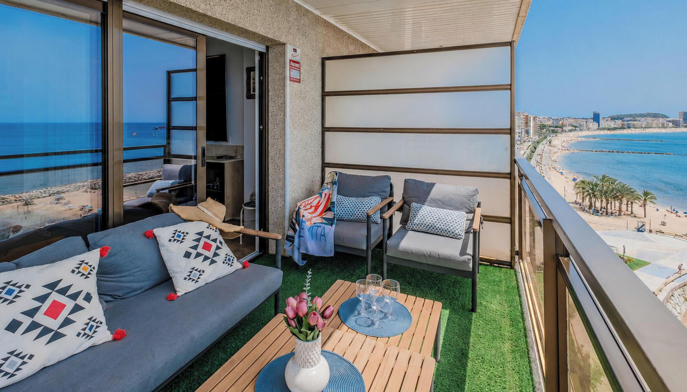 A balcony with a sofa, chairs, and a table with a vase of flowers.