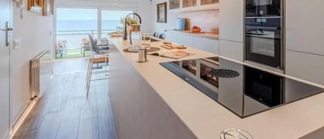 A modern kitchen with a central island, built-in oven, and a view to the outside.