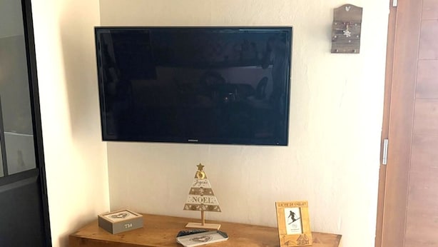 A flat-screen TV mounted on a wall above a wooden console with a small Christmas tree and a framed picture. - T3 Apartment, pets welcome - 74260 Les Gets (Les Gets)