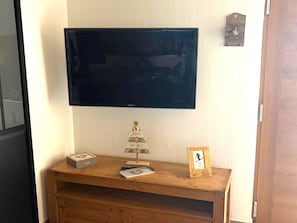 A flat-screen TV mounted on a wall above a wooden console with a small Christmas tree and a framed picture. - T3 Apartment in Les Gets, parking - 4 guests (Les Gets)