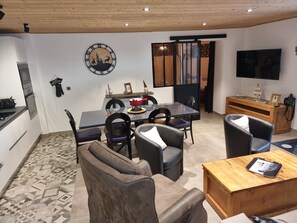 Ein modernes Wohnzimmer mit Essbereich, Holzboden und Fernseher, an der Wand hängt eine Uhr.
